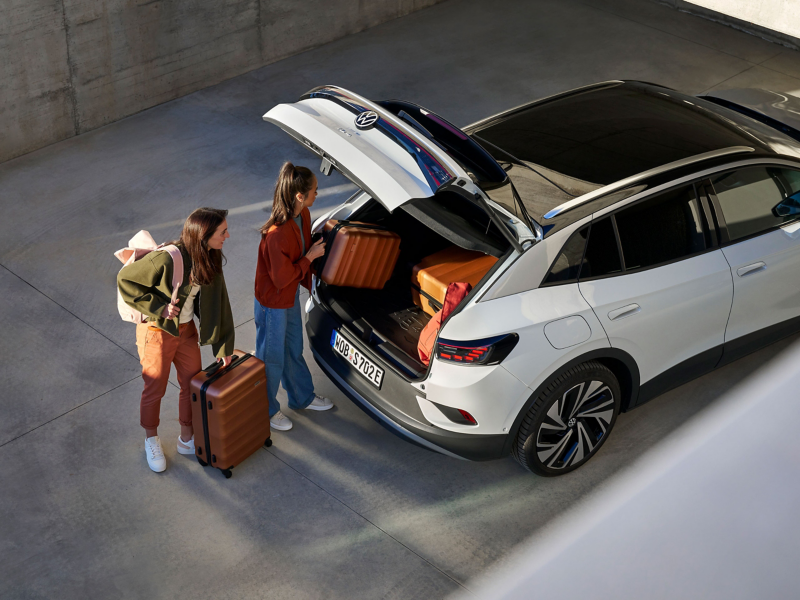 Zwei Frauen beladen Kofferraum eines VW ID.4, Koffer liegen auf Gepäckraumeinlage mit ID.4-Schriftzug aus VW Zubehör Shop