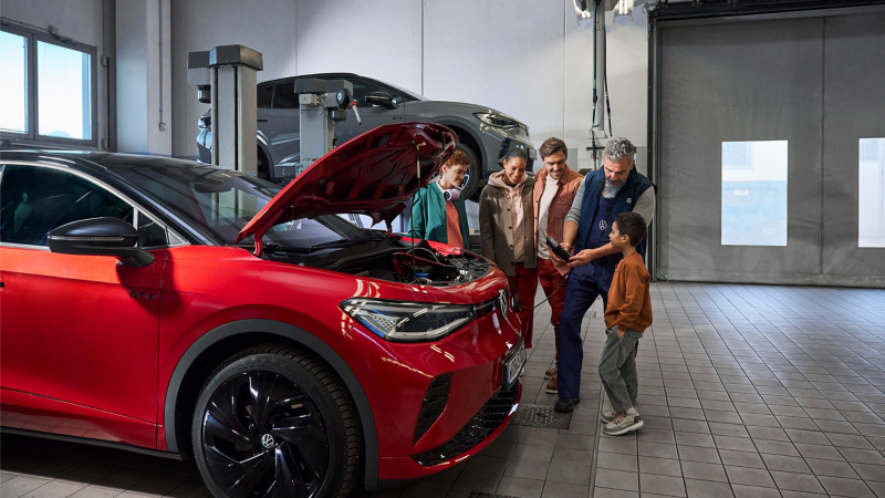 VW ID.5 GTX mit offener Motorhaube: Familie mit VW Servicemitarbeiter beim Batterie Service – VW Reparaturen
