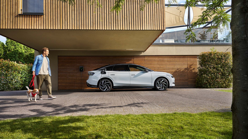 Mann mit Hund läuft an VW ID.7 vorbei, der an ID. Charger Wallbox lädt – VW Zubehör